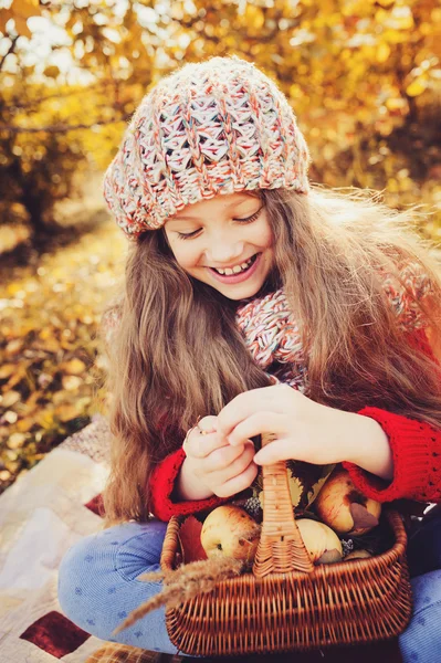 Lyckligt barn flicka i stickad halsduk och tröja med korg på höstens promenad i skogen äta äpplen. Nedgången skörd, mysig stämning. — Stockfoto