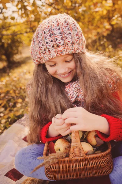 Niña feliz en bufanda de punto y suéter con cesta en otoño paseo en el bosque comiendo manzanas. Cosecha de otoño, ambiente acogedor . — Foto de Stock