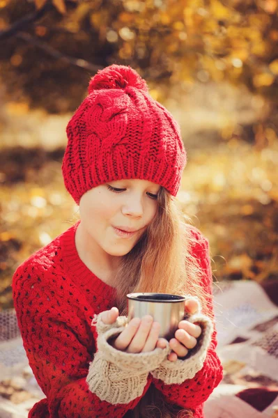 Mutlu çocuk kız sıcak kırmızı örgü şapka ve atkı üzerinde sıcak sonbahar sıcak çay içme termos yürümek. Mevsimlik açık hava etkinlikleri — Stok fotoğraf