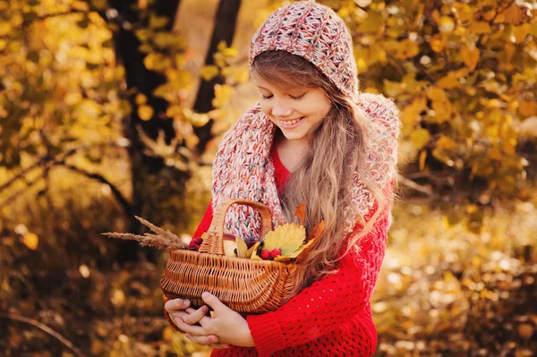 Menina feliz em cachecol de malha e suéter com cesta na caminhada de outono na floresta comendo maçãs. Colheita de outono, humor acolhedor . — Fotografia de Stock