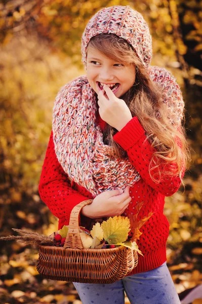 Ευτυχισμένο παιδί κορίτσι στο πλεκτό κασκόλ και τα πουλόβερ με καλάθι με την φθινοπωρινή βόλτα στο δάσος τρώνε μήλα. Συγκομιδή πτώσης, φιλόξενη διάθεση. — Φωτογραφία Αρχείου