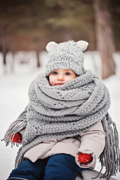 Winter portret van mooie babymeisje in warme oversize gebreide sjaal en muts op de wandeling in de winter van de besneeuwde forest — Stockfoto