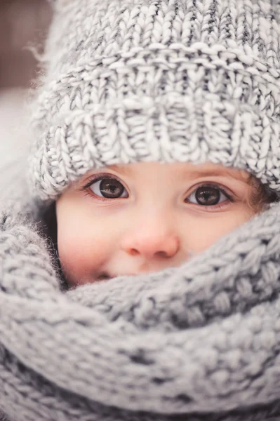 Winter portret van mooie babymeisje in warme oversize gebreide sjaal en muts op de wandeling in de winter van de besneeuwde forest — Stockfoto