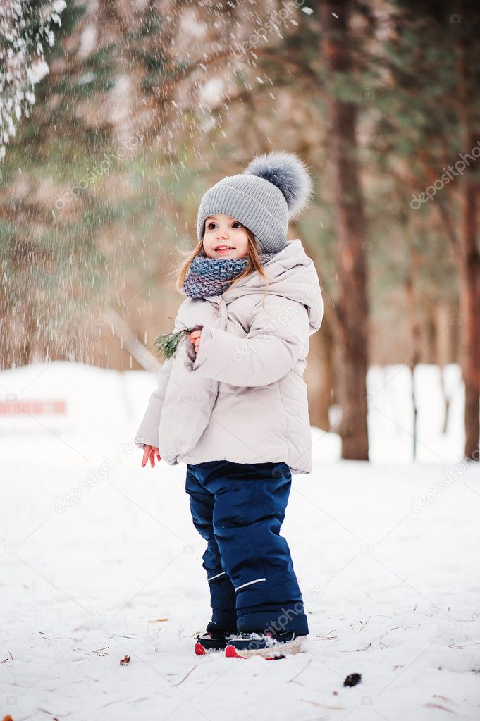 Cute happy baby girl walking in snowy winter forest, spending