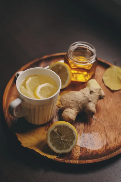 cooking ginger, lemon and honey hot tea in dark rustic interior. Ingredients and cup on wooden background