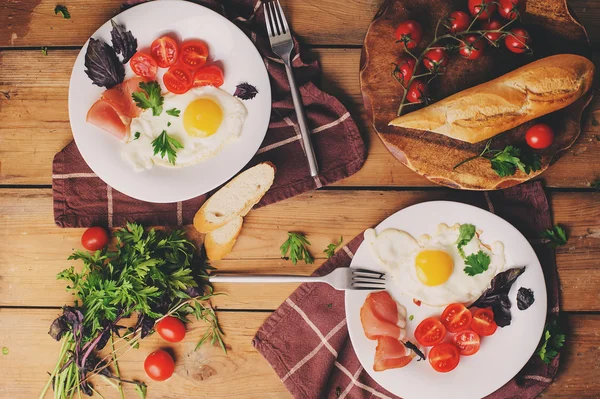 Blick von oben auf Spiegeleier mit Tomaten, Basilikum und Schinken, gedeckter Tisch für zwei, gemütliches Frühstück zu Hause — Stockfoto