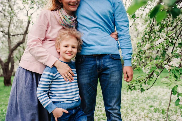 Retrato da mola da família feliz que aprecia feriados no jardim florescendo. Mãe grávida, pai e filho caminhando juntos ao ar livre — Fotografia de Stock