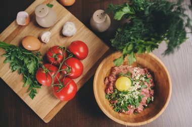 Yumurta, otlar ve ahşap masa üzerinde taze domates çiğ kıyma. Pişirme köfte veya somun rustik mutfak için malzemeler