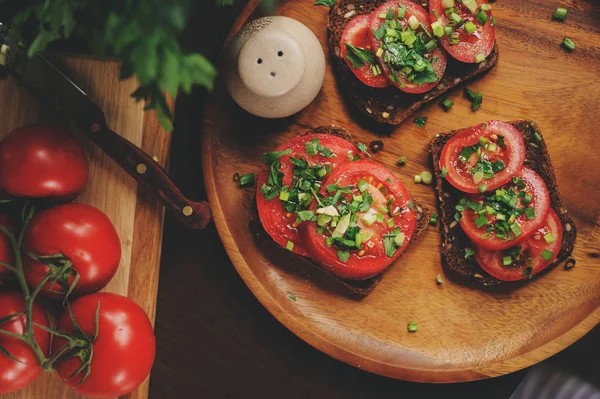 Matlagning toast smörgåsar med färsk tomat, grön lök och fullkornsbröd i mörka rustika interiören på träplatta — Stockfoto