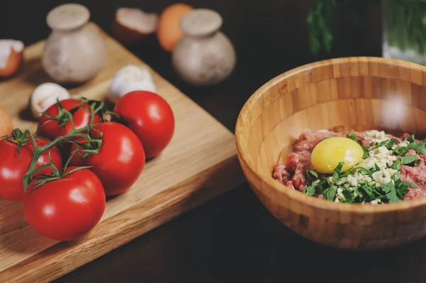 Rå köttfärs med ägg, örter och färska tomater på träbord. Ingredienser för matlagning kött bollar eller limpa i rustikt kök — Stockfoto