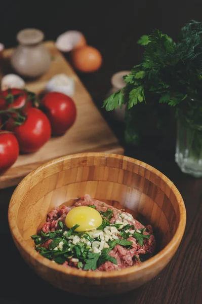 Rå köttfärs med ägg, örter och färska tomater på träbord. Ingredienser för matlagning kött bollar eller limpa i rustikt kök — Stockfoto