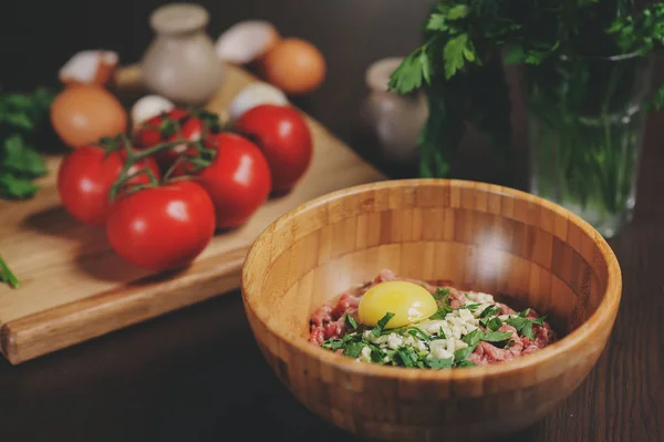 Rå köttfärs med ägg, örter och färska tomater på träbord. Ingredienser för matlagning kött bollar eller limpa i rustikt kök — Stockfoto