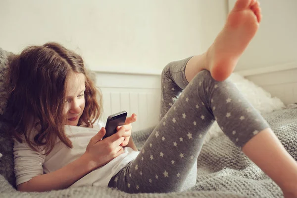 Mädchen spielt Smartphone zu Hause auf dem Bett — Stockfoto