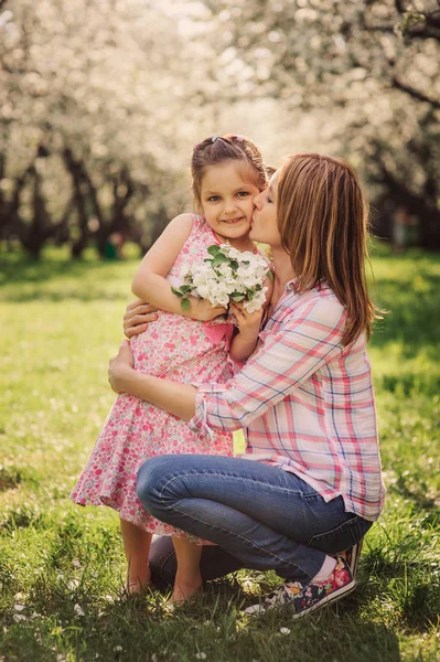 Jarní vertikální portrét happy matka a dítě dcera na zahradě chůze v Kvetoucí třešeň. — Stock fotografie