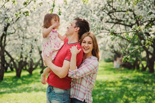 Mãe feliz e pai brincando com a filha da criança na caminhada. Família desfrutando de primavera no jardim florescendo cereja — Fotografia de Stock