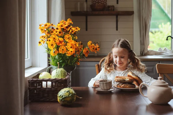 子供の女の子の秋の朝、自宅で朝食を持っていること。現実の生活の国の家で居心地の良いモダンなインテリア。子供のベーグルを食べて、お茶を飲んで. — ストック写真