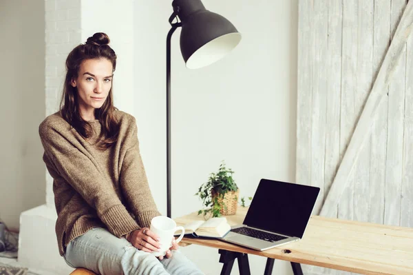 Junge schöne Bloggerin, die morgens mit Laptop und Tasse Kaffee zu Hause online einkauft. Home Office im modernen skandinavischen Interieur — Stockfoto