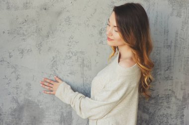 modern daire gri duvar tarafından poz büyük boy örme kazak genç kadın. Rahat yaşam tarzı evde