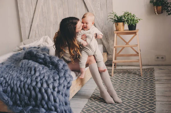 Gelukkig moeder en baby spelen thuis in de slaapkamer. Gezellige familie levensstijl in moderne Scandinavische interieur. — Stockfoto