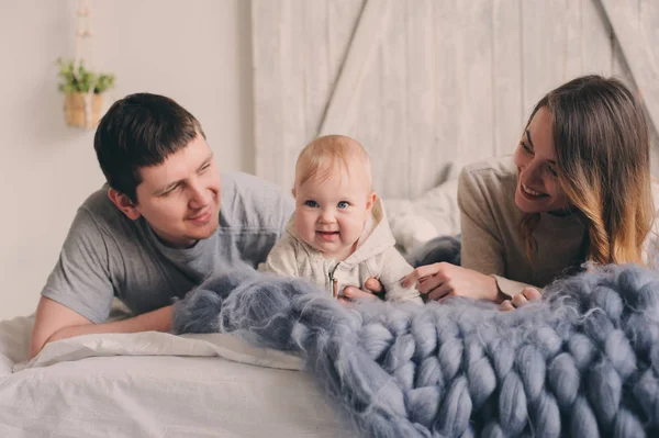 Família feliz brincando em casa na cama. Estilo de vida captura de mãe, pai e bebê no interior escandinavo moderno — Fotografia de Stock