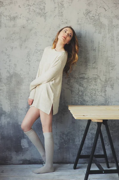 Young woman in oversize knitted sweater posing by the grey wall in modern apartment. Casual lifestyle at home — Stock Photo, Image