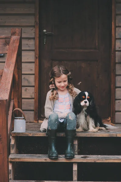Capretto ragazza giocare con il suo cane spaniel, seduto su scale a legno capanna di tronco — Foto Stock