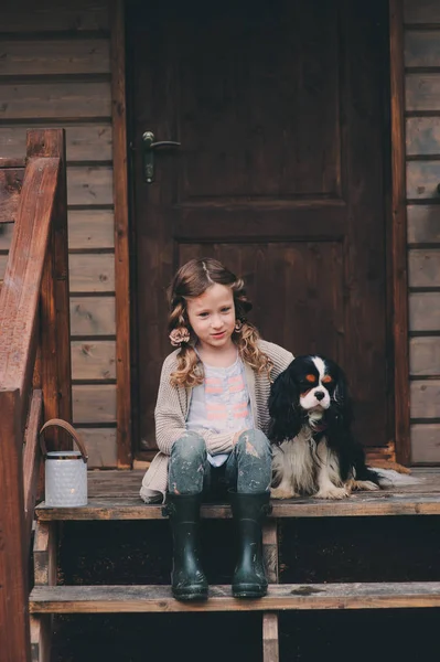 Capretto ragazza giocare con il suo cane spaniel, seduto su scale a legno capanna di tronco — Foto Stock