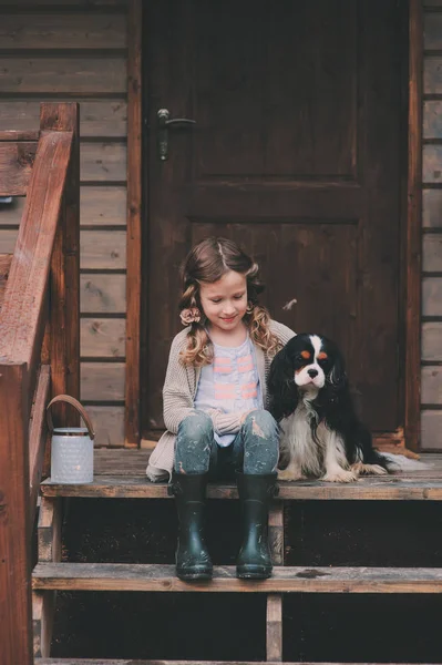 Kid girl playing with her spaniel dog, sitting on stairs at wooden log cabin — Stock Image Kid girl playing with her spaniel dog, sitting on stairs at wooden log cabin Royalty Free Stock Photos