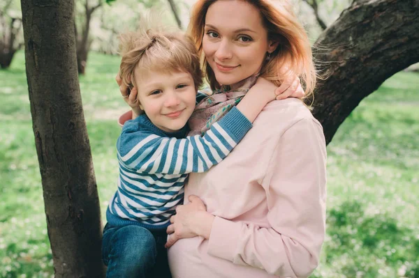 Retrato de primavera de mãe grávida feliz desfrutando de dia quente com filho criança no jardim de maçã florescendo — Fotografia de Stock