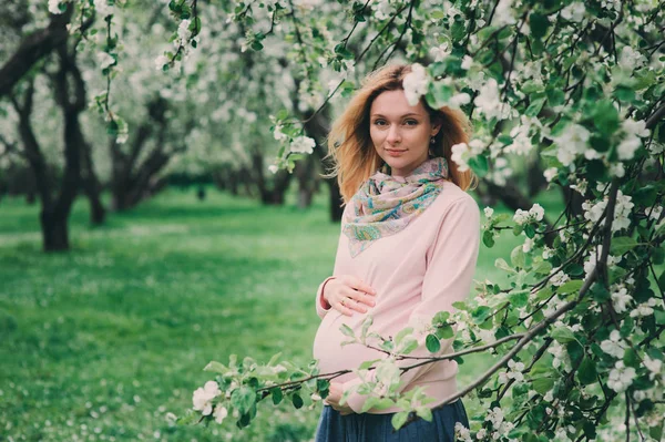 Feliz embarazada rubia hermosa mujer caminando outddor en primavera parque o jardín, posando cerca de árbol en flor — Foto de Stock