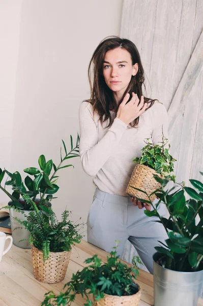 Giovane donna annaffiare vasi da fiori a casa. Serie stile di vita casual in interni scandinavi moderni — Foto Stock