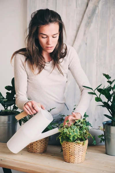 Молодая женщина поливает цветочные горшки дома. Повседневный стиль жизни в современном скандинавском интерьере — стоковое фото