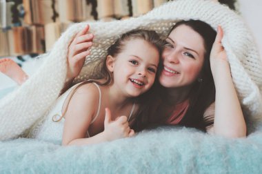 mutlu bir aile evde oynamak. Rahatlatıcı ve having fun yatakta sıcak hafta sonu sabah anne ve yürümeye başlayan çocuk kızı