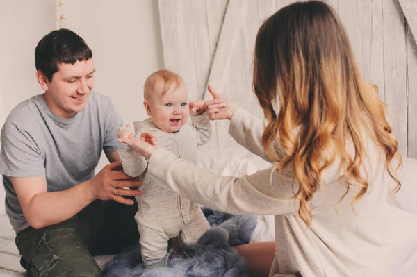 Gelukkige familie thuis speelt op het bed. Vangst van de levensstijl van moeder, vader en baby in moderne Scandinavische interieur — Stockfoto