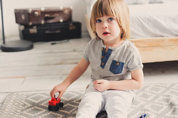 Niño feliz jugando con coches de juguete en casa por la mañana. Estilo de vida casual en el dormitorio — Foto de Stock