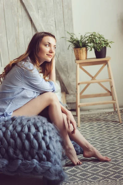 Молодая женщина в пижаме просыпается утром в уютной скандинавской спальне и сидит на кровати с белым постельным бельем. Свободный образ жизни в современном интерьере — стоковое фото