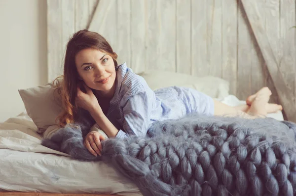 Mujer joven en pijama se despierta por la mañana en el acogedor dormitorio escandinavo y se sienta en la cama con plantas de interior en el fondo. Estilo de vida casual en el interior moderno — Foto de Stock