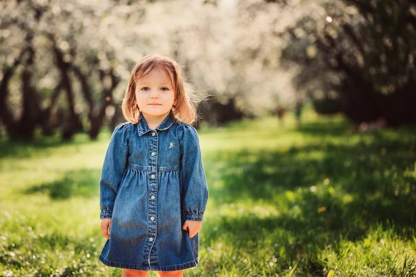 Retrato de primavera da menina pequena bonito em vestido de jeans azul andando no parque florescente ou jardim — Fotografia de Stock