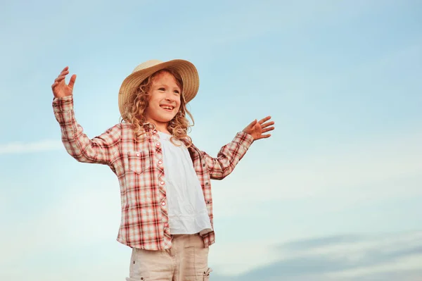 Felice bambina in stile country camicia a quadri e cappello rilassante sul campo estivo con pile di fieno — Foto Stock