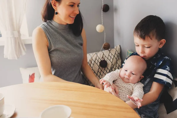 Счастливая молодая мать завтракает на кухне со своей маленькой дочерью и маленьким сыном — стоковое фото