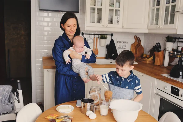 happy family baking together in modern white kitchen. Mother, son and baby daughter cooking in cozy weekend morning at home