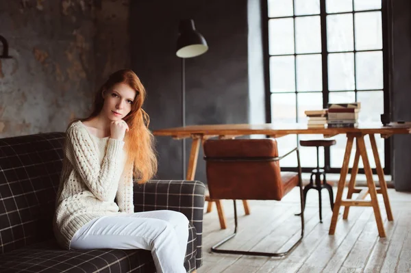 Young beautiful redhead woman relaxing at home in the autumn cozy evening and reading book on couch — Stock Photo, Image