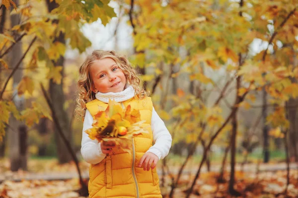 Söta småbarn flicka som leker med lämnar i höst park på promenad, klädd i mode gul outfit — Stockfoto