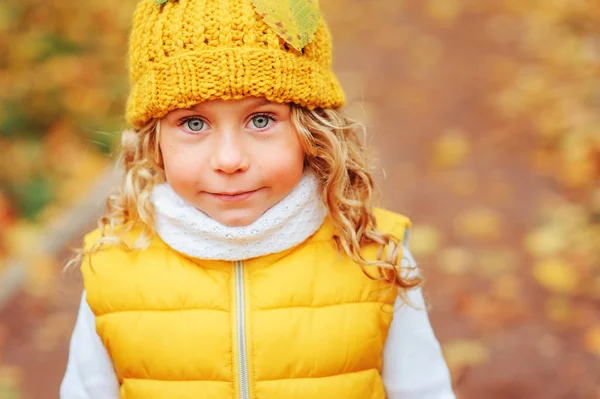 Мила дівчинка-малюк грає з листям в осінньому парку на прогулянці, одягнена в модний жовтий одяг — стокове фото