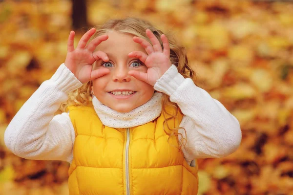 Bonito criança menina brincando com folhas no outono parque no passeio, vestindo moda roupa amarela — Fotografia de Stock