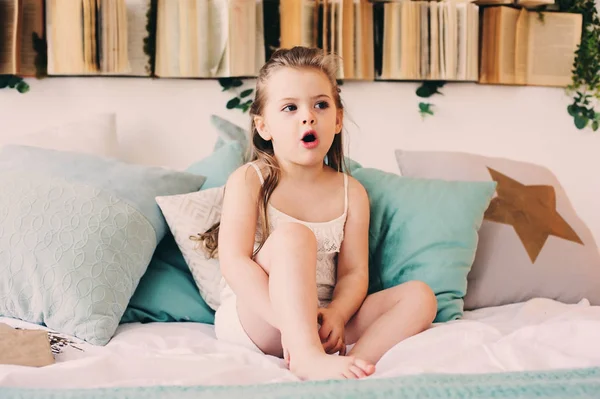 Aranyos boldog kisgyermek lány pizsama ágy ül. Gyermek játszik otthon, alkalmi életmód elfog. — Stock Fotó