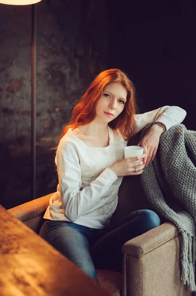 Jeune belle rousse femme détente sur chaise à la maison avec une tasse de thé ou de cacao . — Photo