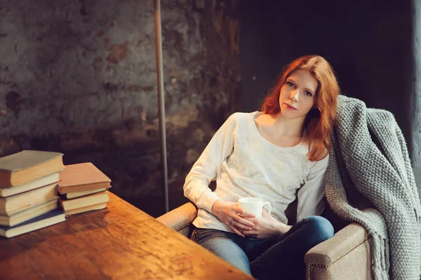 Joven hermosa pelirroja mujer relajarse en la silla en casa con taza de té o cacao . — Foto de Stock