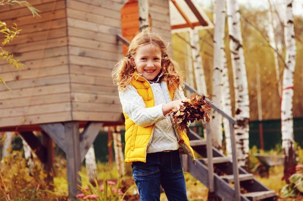 Happy child girl playing little gardener in autumn and picking leaves into basket. Seasonal garden work. Backyard cleaning. — Stock Photo, Image