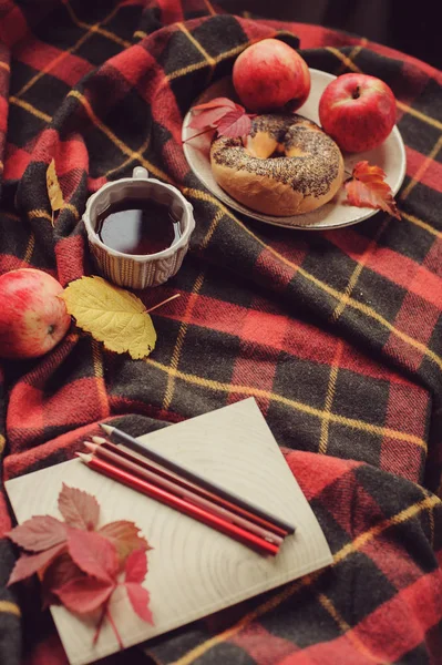 Top view of cozy autumn morning at home. Breakfast with pot of tea and bagel with apples on woolen plaid blanket.